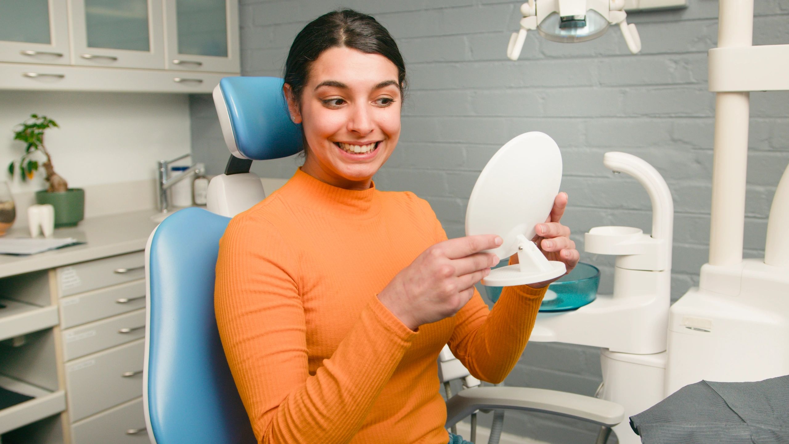 Smiling dental patient checking her teeth in a mirror after treatment
